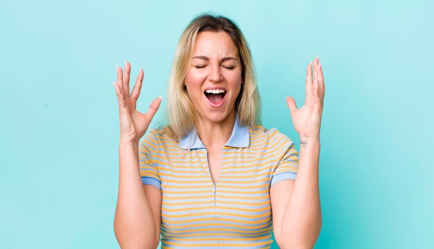 Jolie femme blonde hurlant furieusement stressée et agacée avec les mains en l'air en disant pourquoi moi