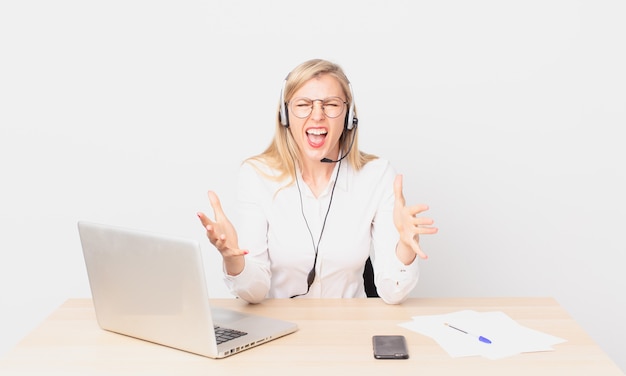 Jolie femme blonde jeune femme blonde semblant en colère, agacée et frustrée et travaillant avec un ordinateur portable