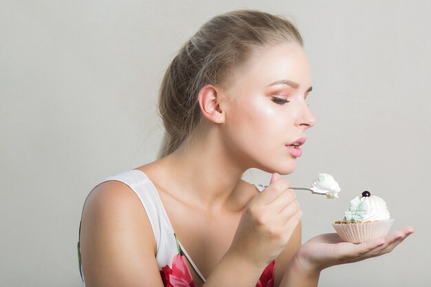 Jolie femme blonde mangeant un délicieux dessert sucré avec de la crème au beurre