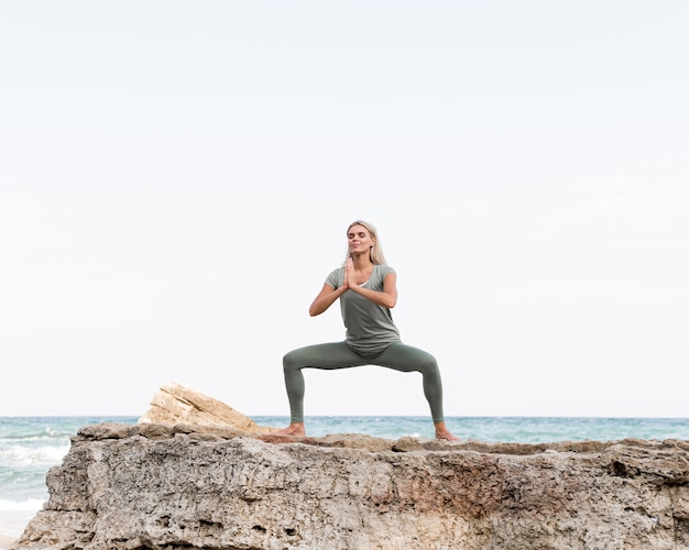 Jolie femme blonde pratiquant le yoga à la plage
