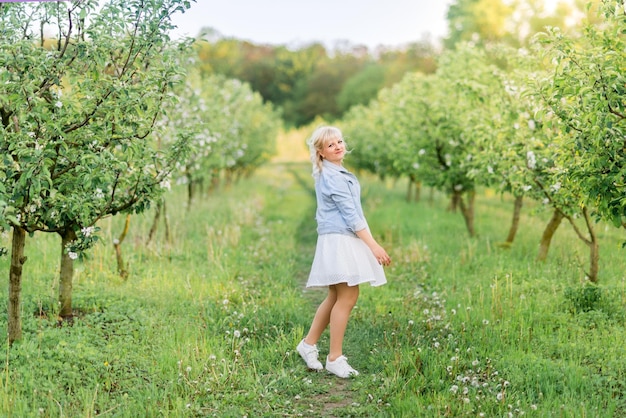 Jolie femme blonde près d'un pommier en fleurs Une fille dans un jardin de printemps