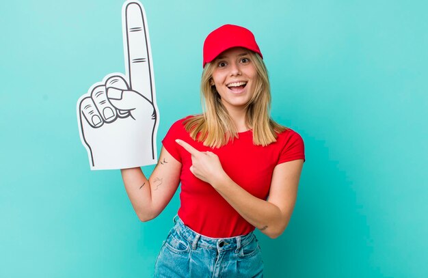 Jolie femme blonde qui a l'air excitée et surprise en montrant le concept de fan numéro un du côté