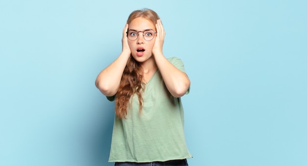 Jolie femme blonde à la recherche désagréablement choquée, effrayée ou inquiète, bouche grande ouverte et couvrant les deux oreilles avec les mains