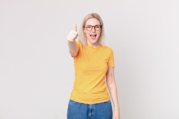 Jolie femme blonde se sentant fière, souriant positivement avec les pouces vers le haut