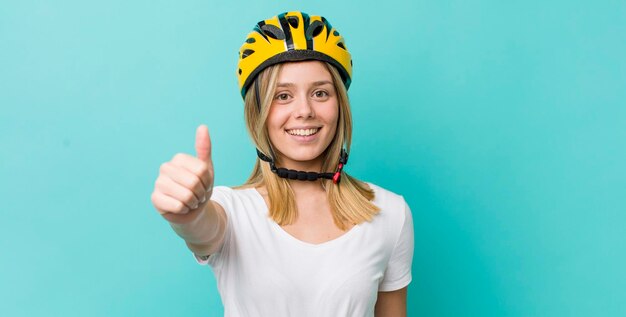 Jolie femme blonde se sentant fière de sourire positivement avec le concept de vélo pouce en l'air