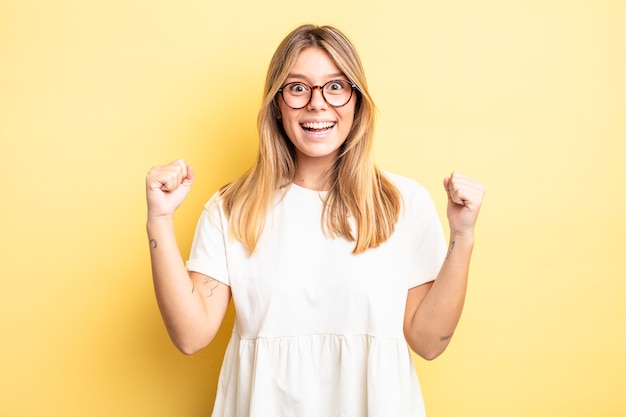 Jolie femme blonde se sentant heureuse, surprise et fière, criant et célébrant le succès avec un grand sourire