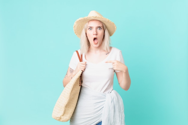 Jolie femme blonde semblant choquée et surprise avec la bouche grande ouverte, pointant vers soi. concept d'été