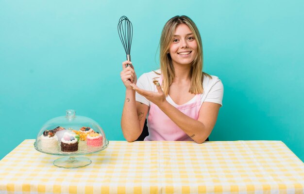 Jolie femme blonde souriant joyeusement se sentant heureuse et montrant un concept concept de gâteau fait maison