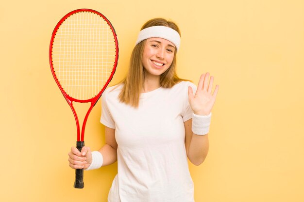 Jolie femme blonde souriante agitant joyeusement la main vous accueillant et vous saluant concept de tennis