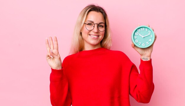 Jolie femme blonde souriante et amicale montrant le concept de réveil numéro trois