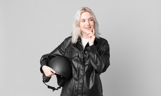 Jolie femme blonde souriante avec une expression heureuse et confiante avec la main sur le menton. concept de motard