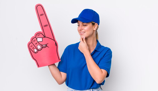 Jolie femme blonde souriante avec une expression heureuse et confiante avec la main sur le menton numéro un concept de ventilateur à la main