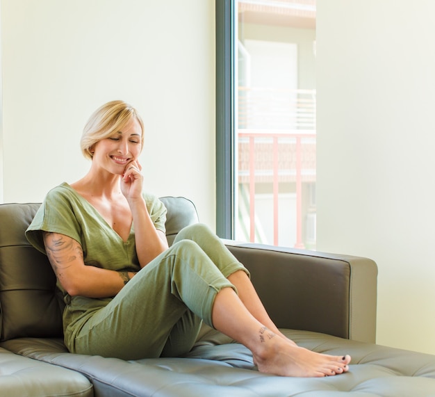 Jolie femme blonde souriante avec une expression heureuse et confiante avec la main sur le menton, se demandant et regardant sur le côté