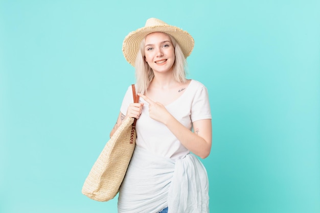 Jolie femme blonde souriante joyeusement, se sentant heureuse et pointant sur le côté. concept d'été