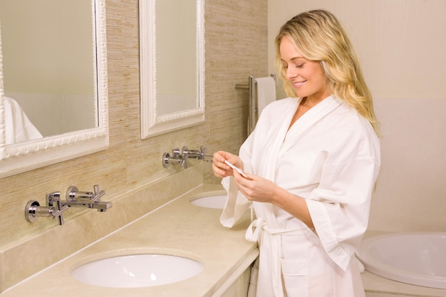 Jolie femme blonde souriante regardant un test de grossesse dans la salle de bain