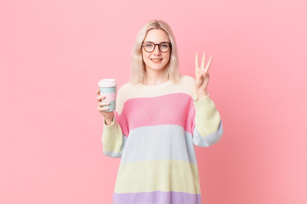 Jolie femme blonde souriante et semblant amicale, montrant le numéro trois. concept de café