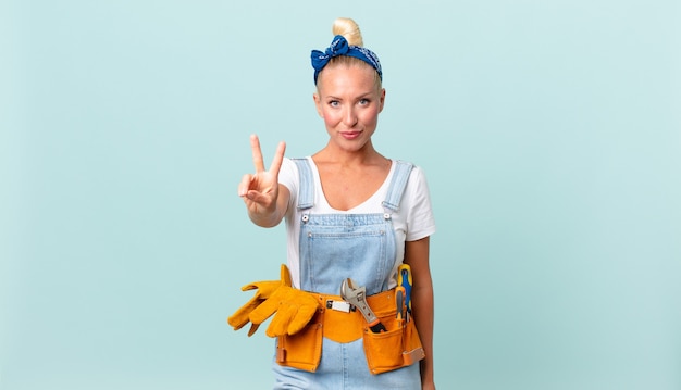 Jolie femme blonde souriante et semblant heureuse, gesticulant la victoire ou la paix et réparant le concept de maison