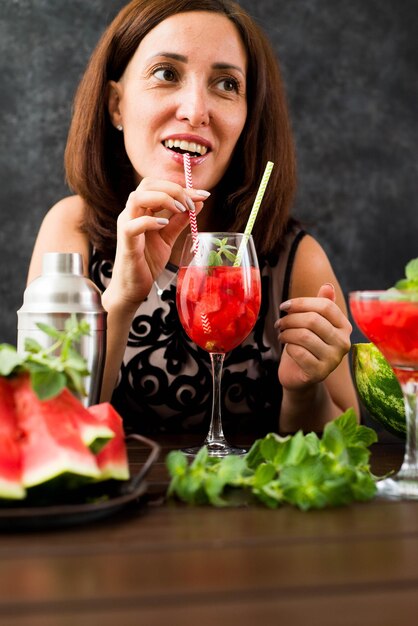 Jolie femme boit un cocktail de pastèque sur fond sombre