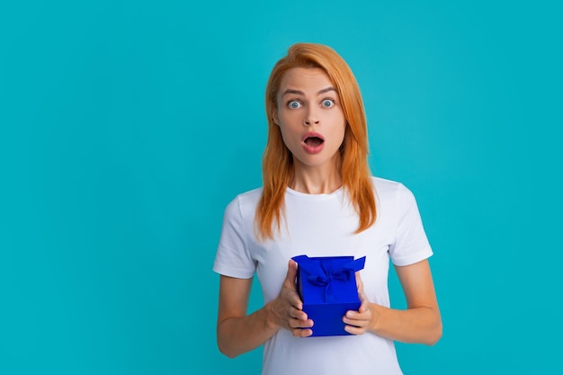 Jolie femme avec boîte présente posant avec l'expression du visage surpris sur fond gris Fille tenant un cadeau décoré de ruban Expressions faciales expressives avec un visage surpris