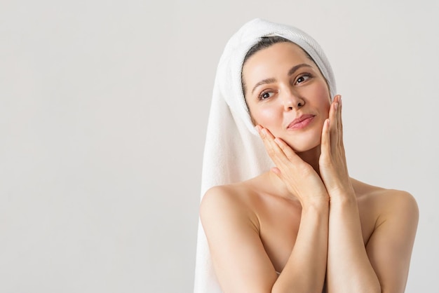 Une jolie femme avec une bonne peau tient ses joues et regarde dans la beauté de la cosmétologie du spa miroir