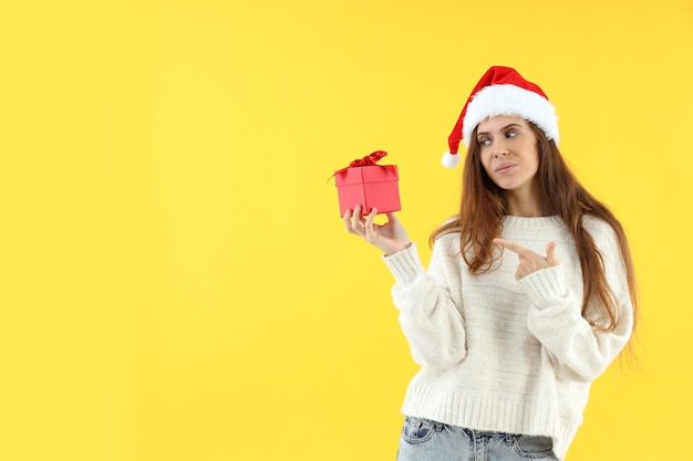 Jolie femme en bonnet de Noel détient une boîte-cadeau sur fond jaune