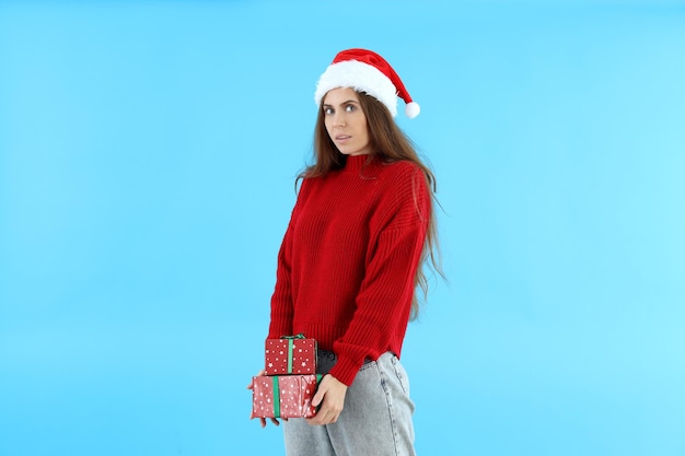 Jolie femme en bonnet de Noel détient des coffrets cadeaux sur fond bleu