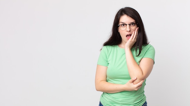 Jolie femme bouche bée sous le choc et l'incrédulité, la main sur la joue et le bras croisés, se sentant stupéfaite et étonnée