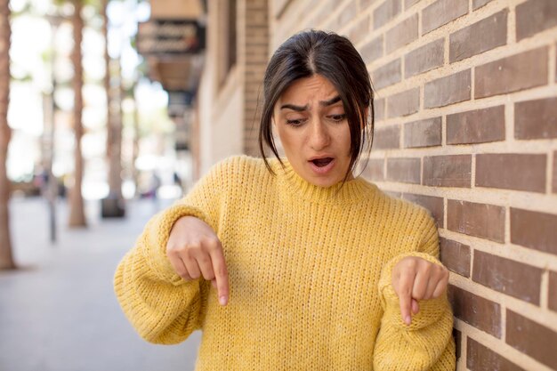 jolie femme avec la bouche ouverte pointant vers le bas avec les deux mains semblant choquée, étonnée et surprise