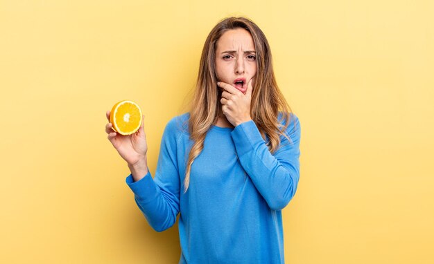 Jolie femme avec la bouche et les yeux grands ouverts et la main sur le menton tenant la moitié d'orange