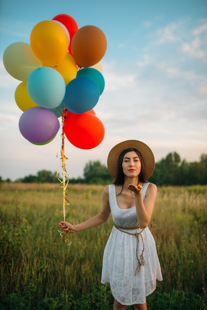 Jolie femme avec bouquet de ballons colorés envoie un baiser