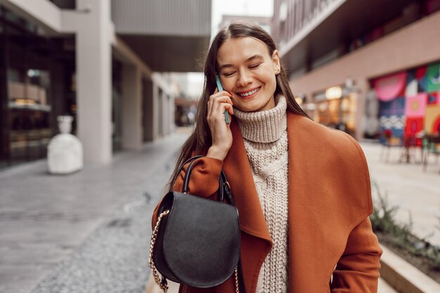 Jolie femme brune en manteau marron parlant au téléphone dans la ville