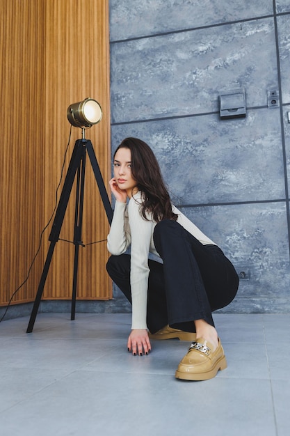 Jolie femme brune en pantalon noir et mocassins marron posant en studio