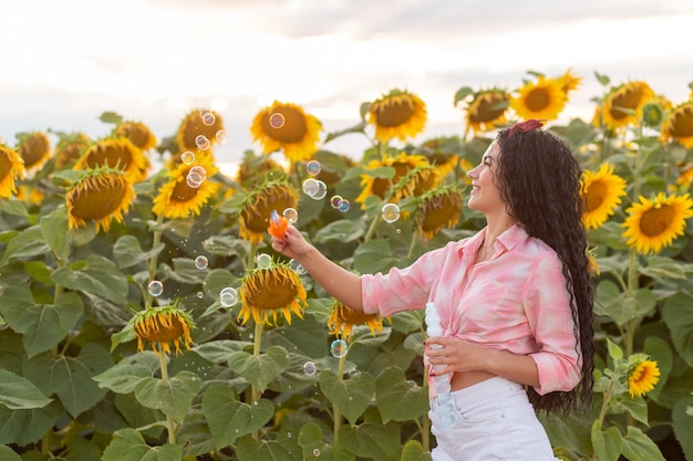 Jolie femme brune soufflant des bulles de savon. Beau champ de tournesols sur fond.