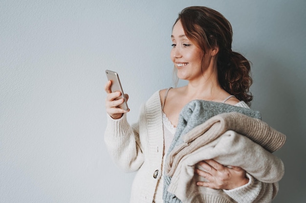 Jolie femme brune souriante d'âge moyen avec des chandails tricotés à l'aide de mobiles à la maison des vibrations confortables