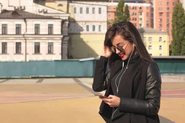 Jolie femme brune souriante regardant une vidéo sur téléphone portable, debout dans la rue