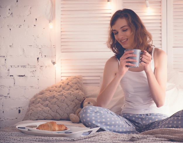 Jolie femme buvant du café assis sur le lit à la maison