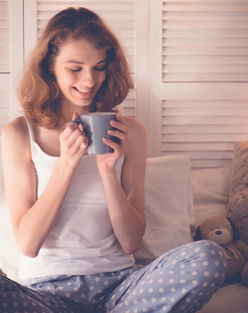 Jolie femme buvant du café assis sur le lit à la maison