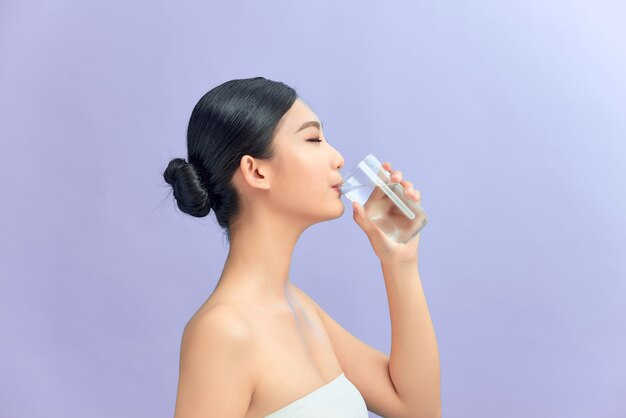 Jolie femme buvant de l'eau sur fond violet