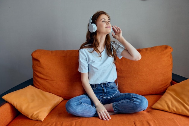 Jolie femme sur le canapé orange écoutant de la musique avec des technologies d'écouteurs