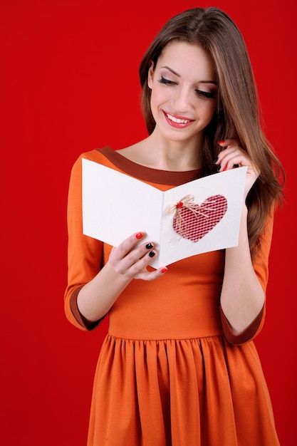 Jolie femme avec carte postale, sur fond rouge
