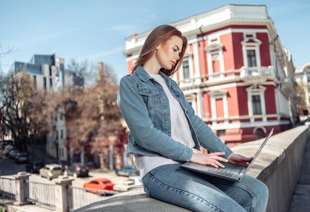 Photo jolie femme caucasienne aux cheveux longs utilisant un ordinateur portable dans la ville