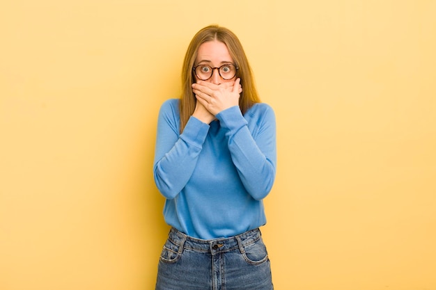 Jolie femme caucasienne couvrant la bouche avec les mains avec une expression choquée et surprise, gardant un secret ou disant oups