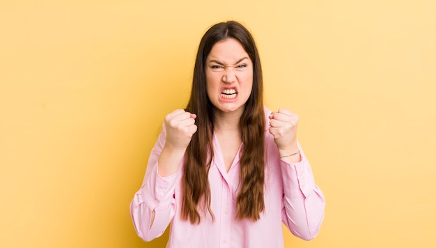 Jolie femme caucasienne criant agressivement avec un regard en colère agacé et frustré et des poings serrés se sentant furieux