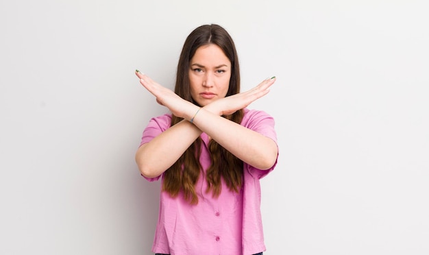 Jolie femme caucasienne qui a l'air ennuyée et malade de votre attitude en disant assez de mains croisées à l'avant pour vous dire d'arrêter