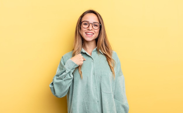 Jolie femme caucasienne qui a l'air heureuse, fière et surprise, pointant joyeusement vers le sentiment de confiance et de noblesse