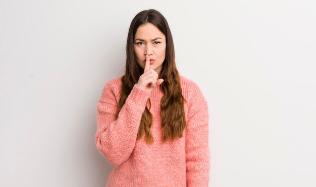 Jolie femme caucasienne à la recherche sérieuse et croisée avec le doigt appuyé sur les lèvres exigeant le silence ou le silence en gardant un secret