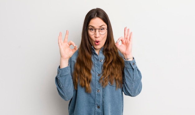 Jolie femme caucasienne se sentant choquée, étonnée et surprise, montrant son approbation en faisant signe d'accord avec les deux mains