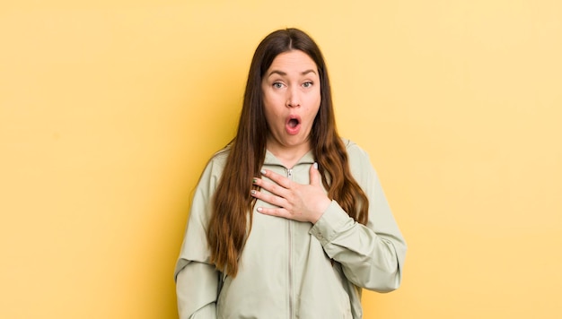 Jolie femme caucasienne se sentant choquée et surprise souriante prenant la main à cœur heureuse d'être celle ou montrant de la gratitude