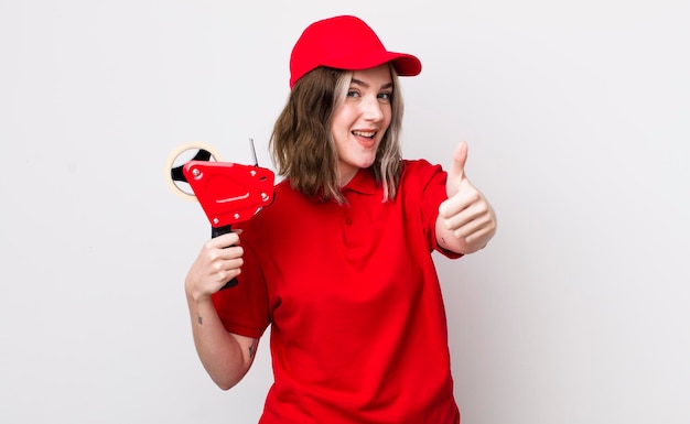 Jolie femme caucasienne se sentant fière de sourire positivement avec le concept d'emballeur de pouces vers le haut