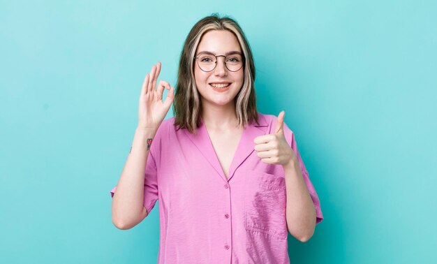 Jolie femme caucasienne se sentant heureuse, étonnée, satisfaite et surprise, montrant d'accord et pouce vers le haut des gestes en souriant